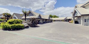 A row of modern buildings with a paved driveway, surrounded by greenery and palm trees. - Capri on Fenton (Rotorua)