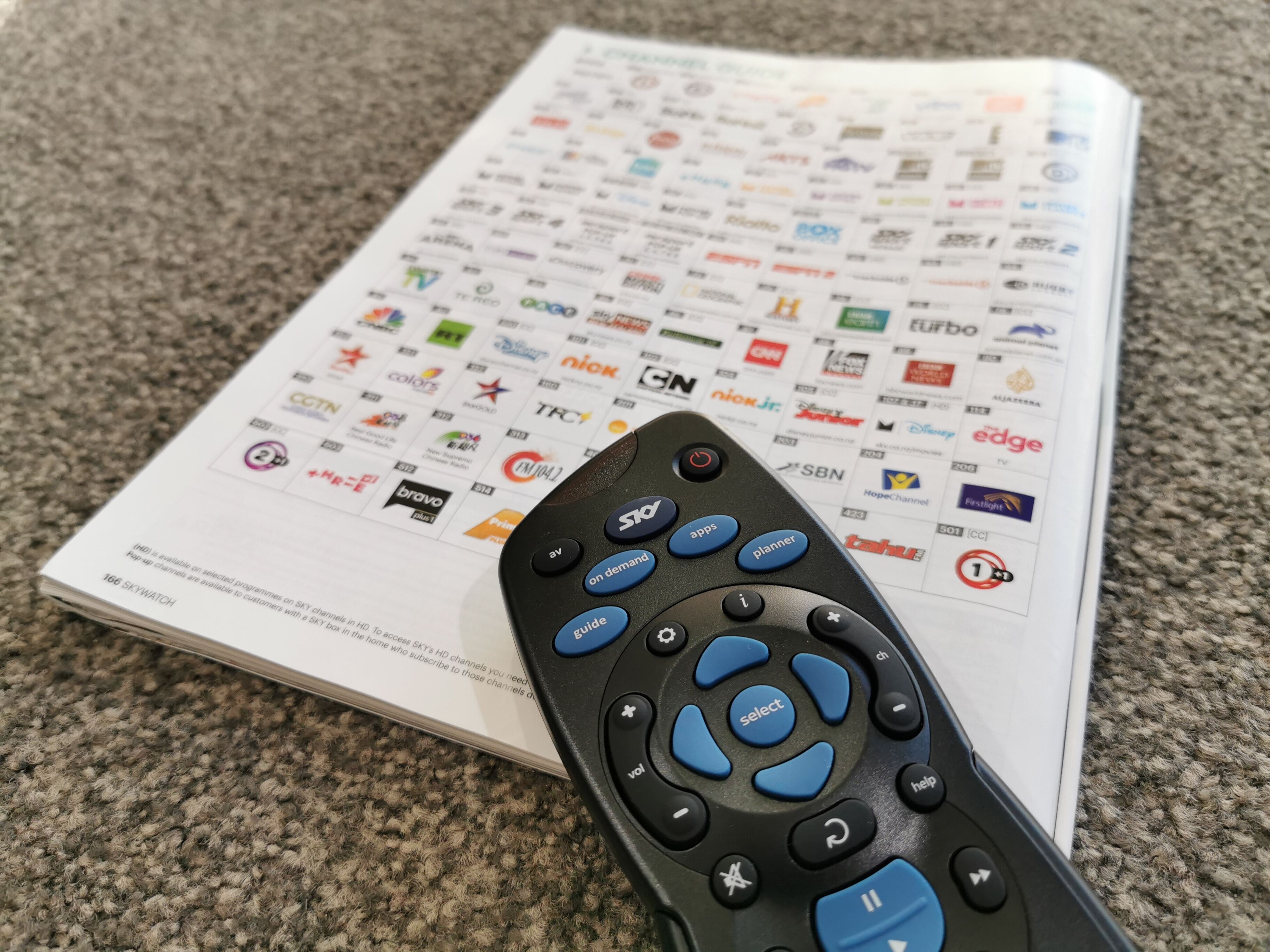 A remote control and a TV guide on a carpeted surface.