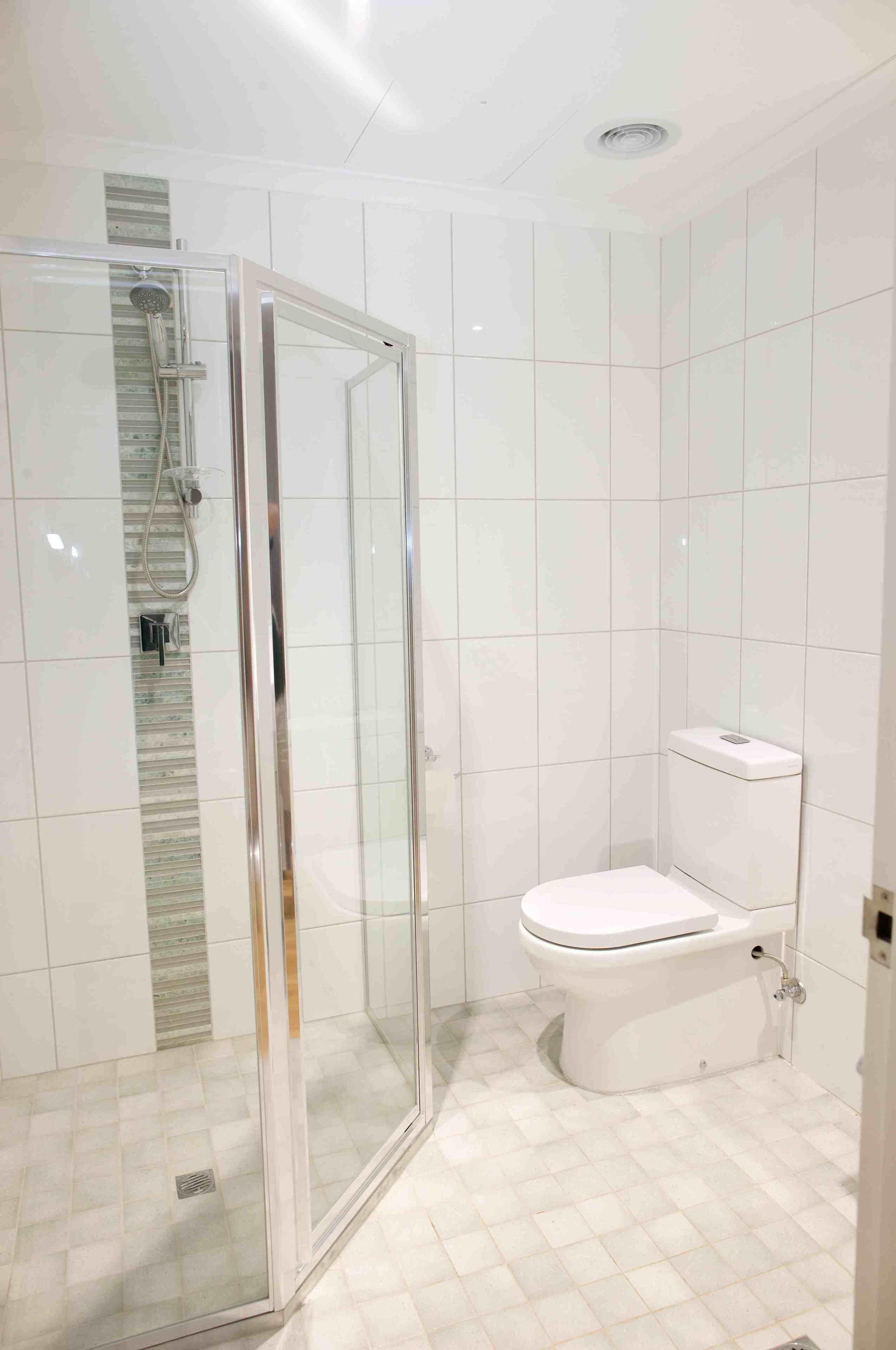 Baño con ducha envuelta en vidrio, inodoro y paredes de azulejos blancos.