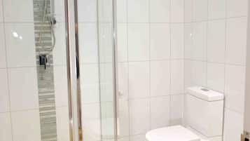 Baño con ducha envuelta en vidrio, inodoro y paredes de azulejos blancos.