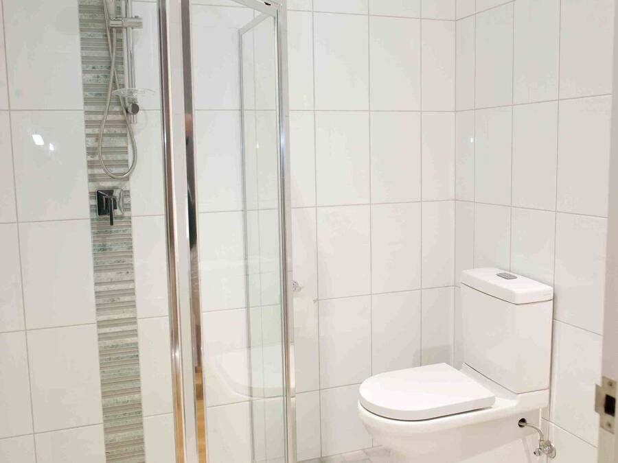 A bathroom with a glass-enclosed shower, a toilet, and white tiled walls.