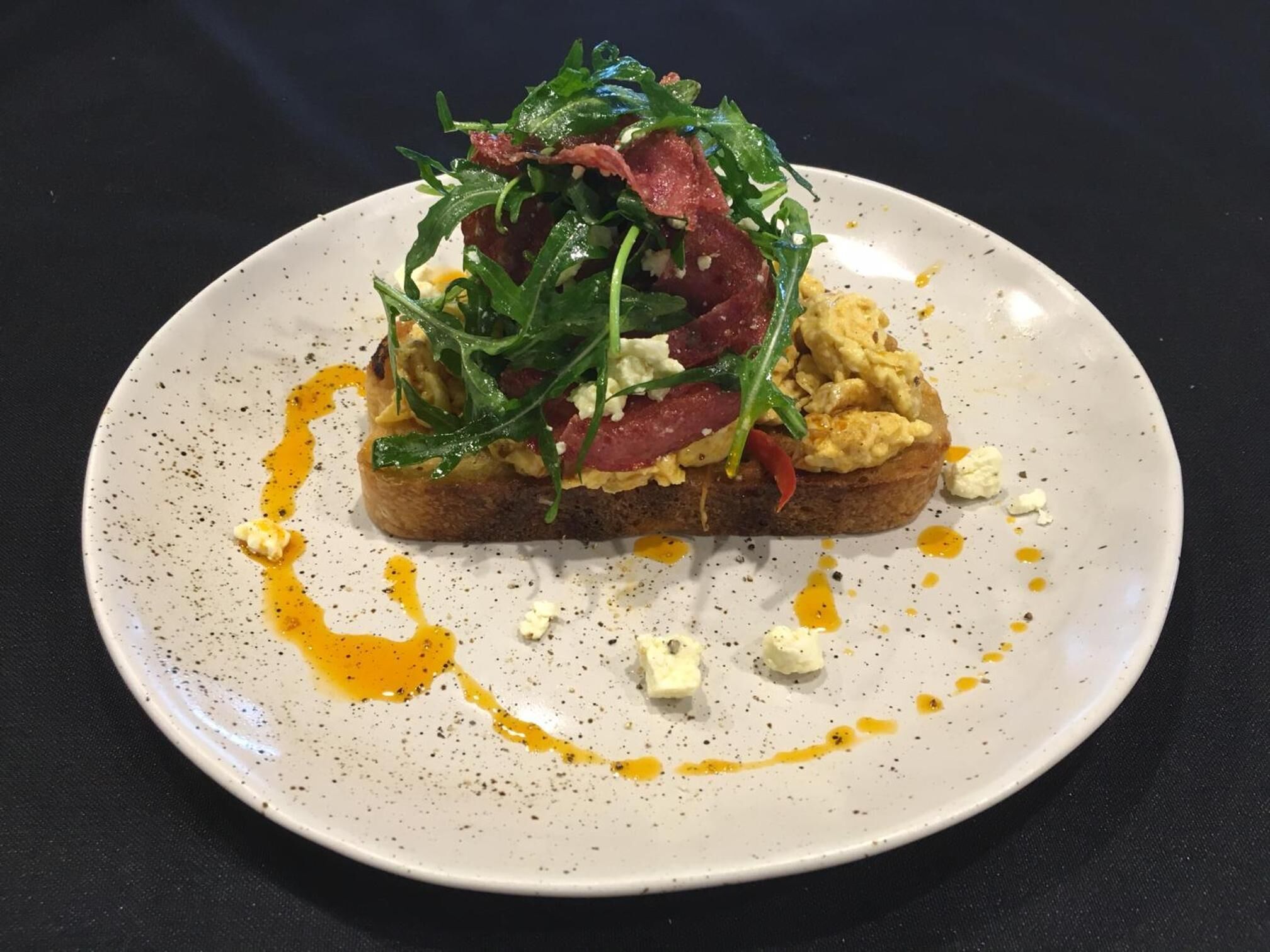 A plate with scrambled eggs, arugula, and a piece of toast.