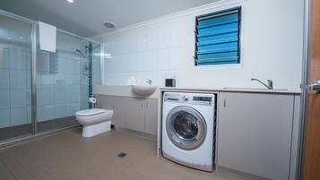 A modern bathroom with a glass shower enclosure, a toilet, a washing machine, and a sink.