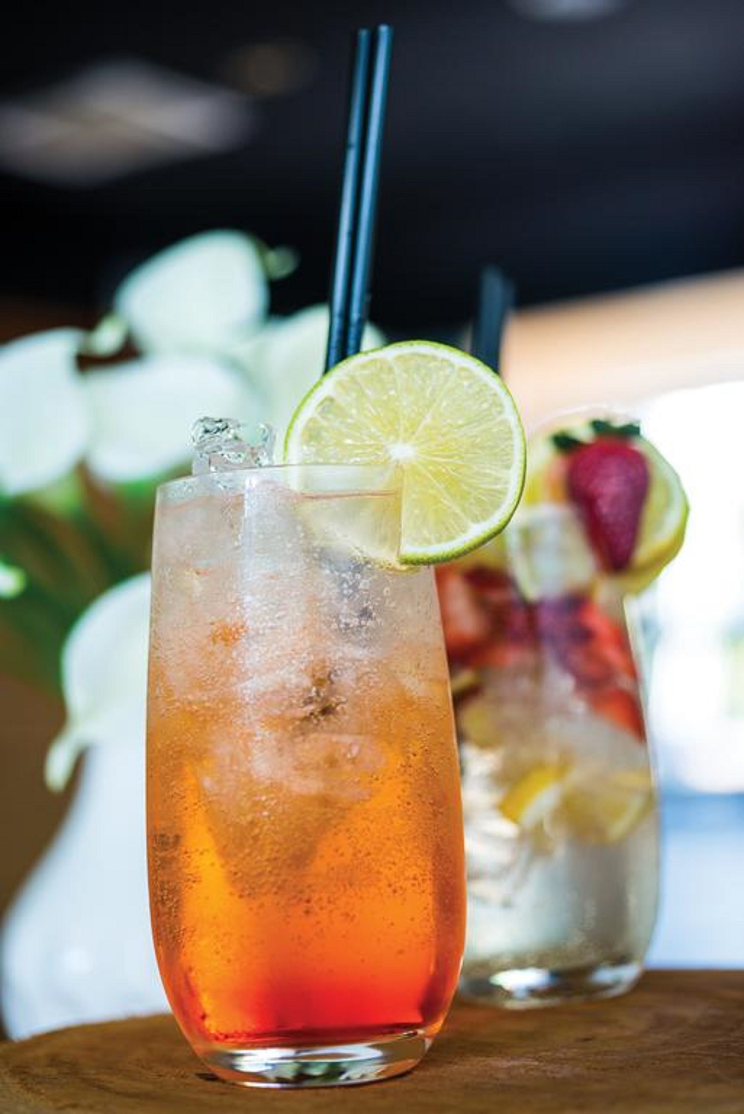 A glass of iced beverage with a lime slice garnish, ice cubes, and a straw, placed on a wooden surface.