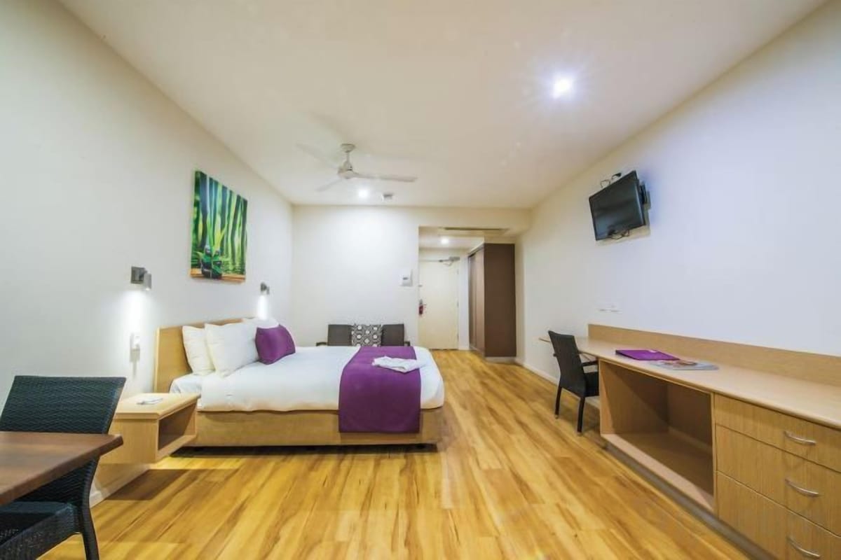 A hotel room with a bed, desk, chair, and a television on the wall.