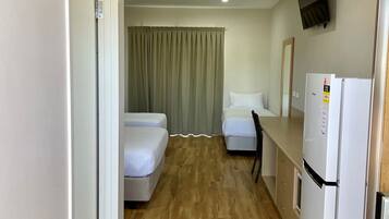 A hotel room with two beds, a ceiling fan, a TV mounted on the wall, and a refrigerator.
