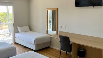 Habitación de hotel con cama, escritorio, silla, televisión, ventilador de techo y ventana con vistas a zonas verdes.