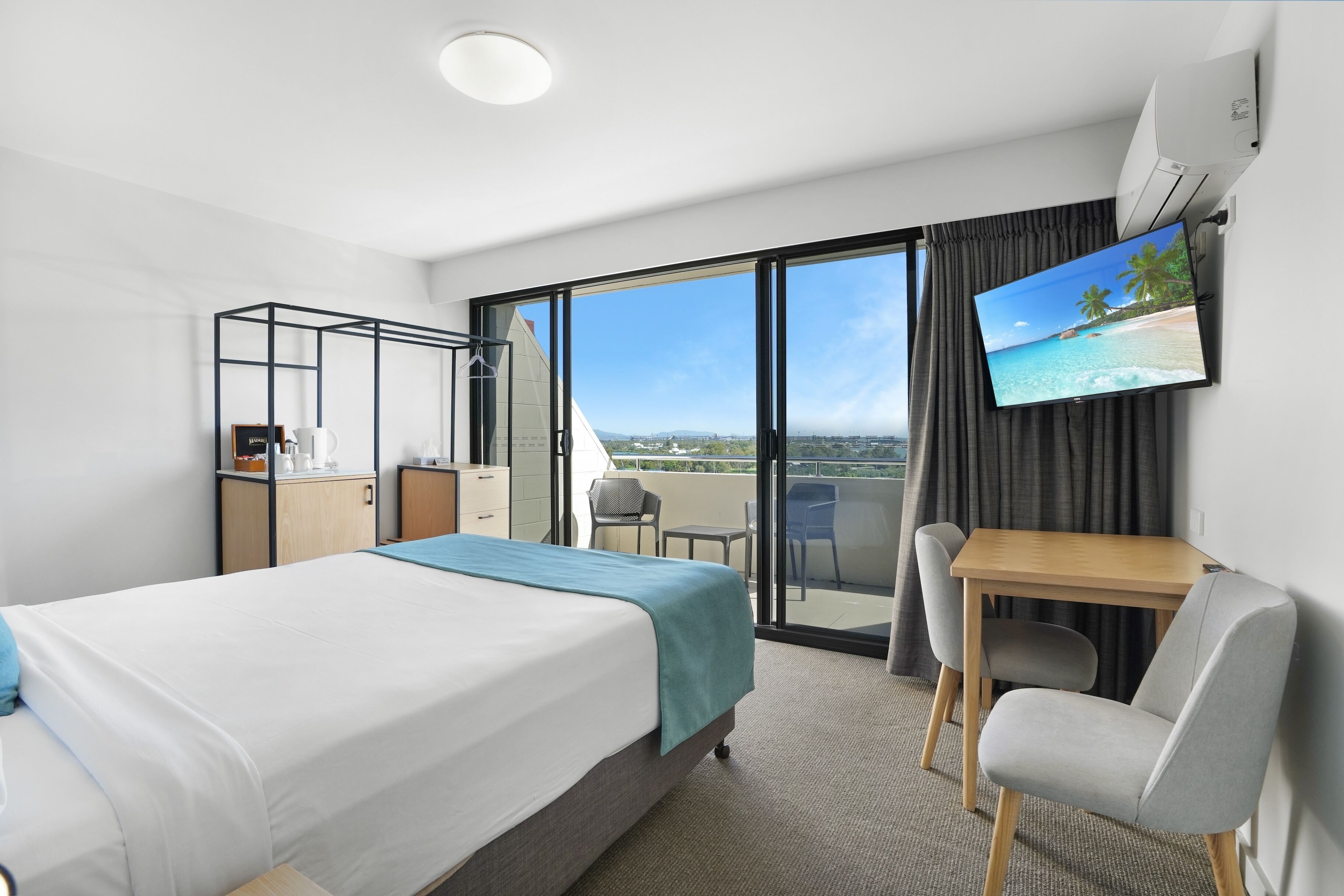 A hotel room with a bed, a desk, a chair, a TV, and a balcony with a view.