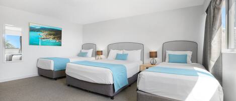 A hotel room with three beds, a large window with curtains, a painting on the wall, and a carpeted floor.