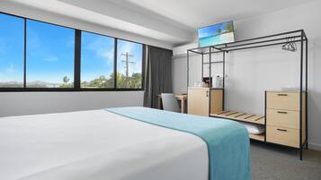 Quarto de hotel com uma cama grande, uma escrivaninha com cadeira, um guarda-roupa e uma televisão na parede.