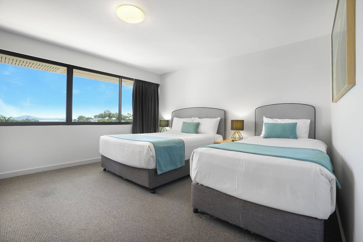 A hotel room with two beds, a large window, and a view of the outdoors.
