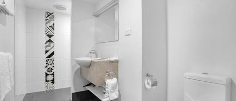 Un baño moderno con ducha, lavabo, inodoro y pared de azulejos con diseño.