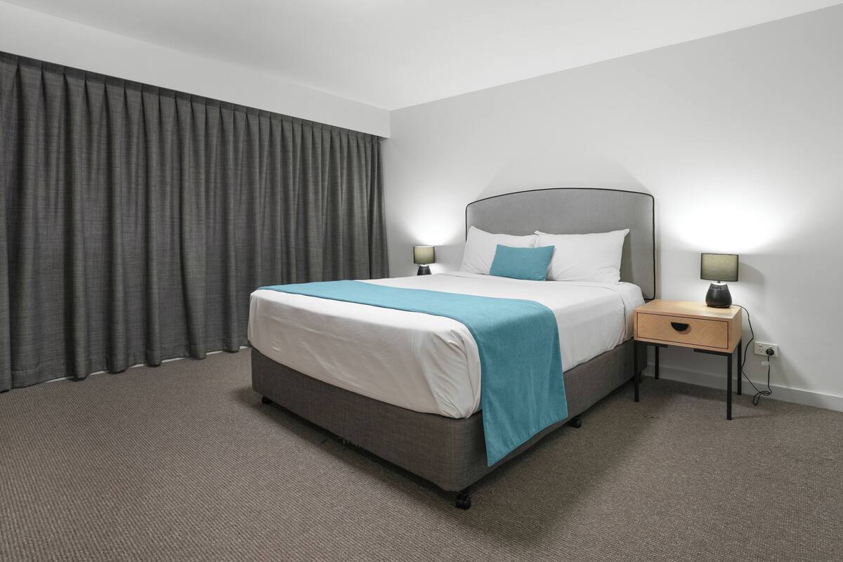 A hotel room with a bed, nightstands, a lamp, and a curtain.