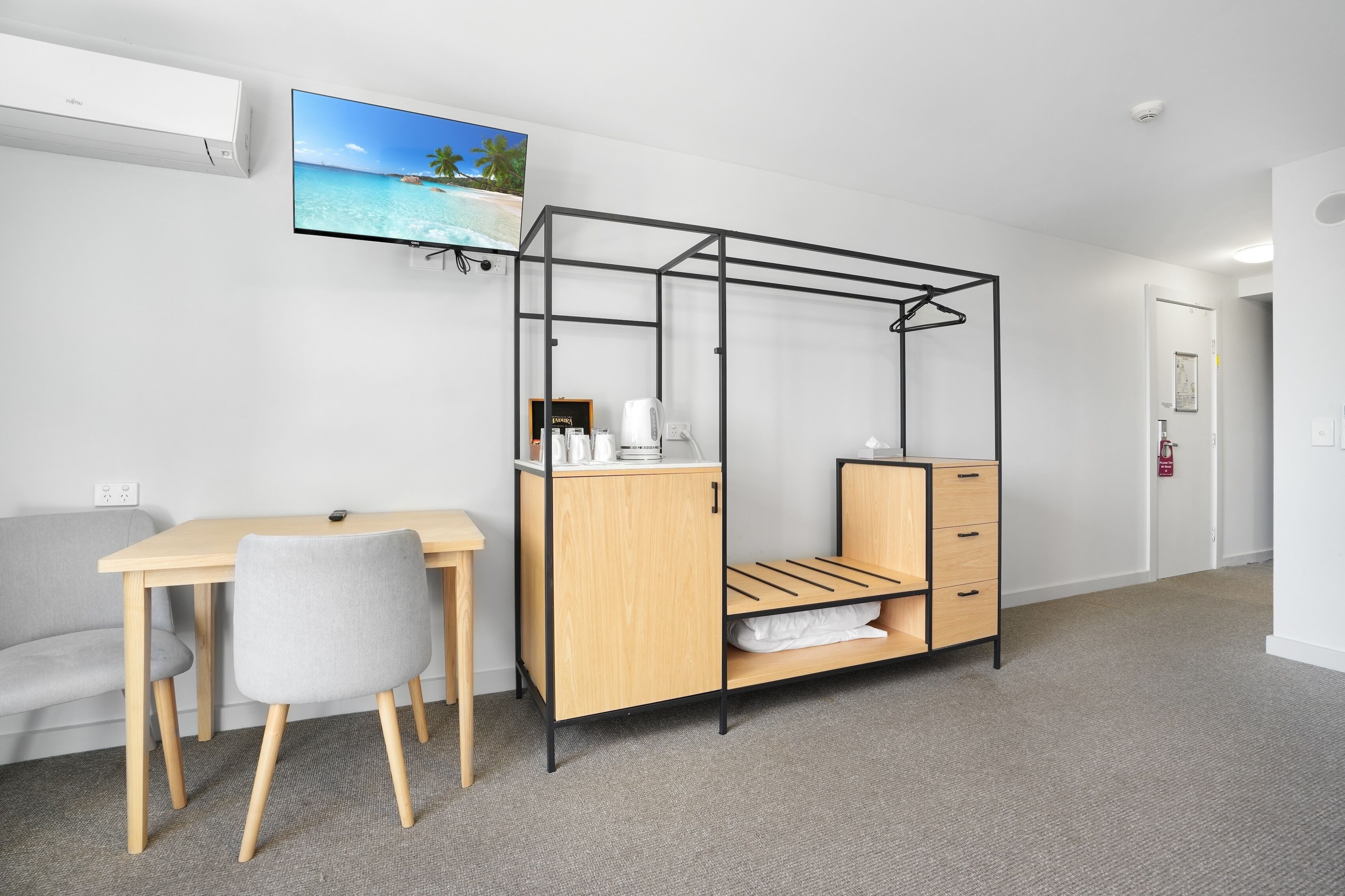 A modern room with a bed, desk, and chair, featuring a beach view on the wall.