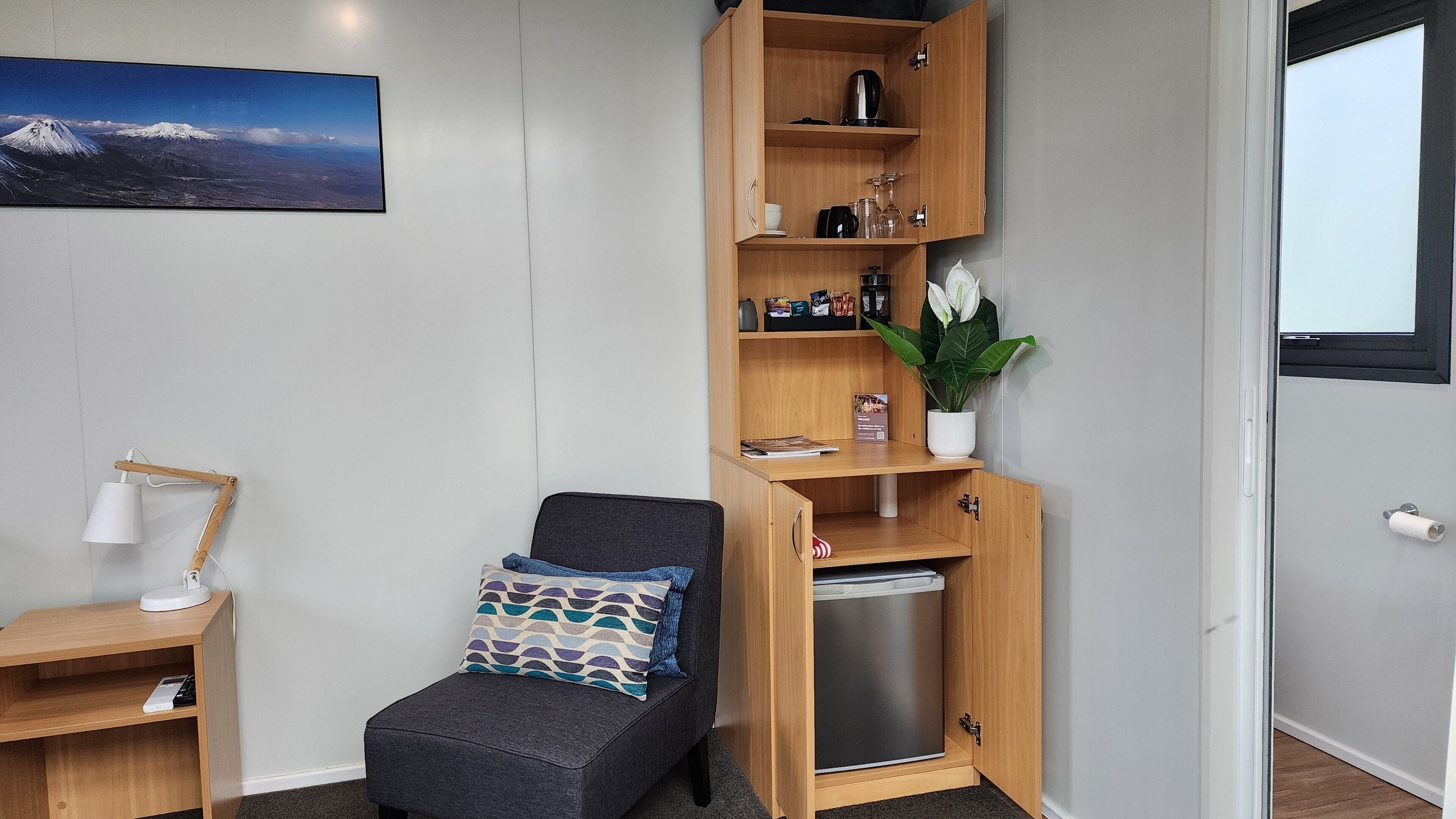 A compact living space with a sofa, a wooden cabinet with shelves, a small desk, and a wall-mounted lamp.