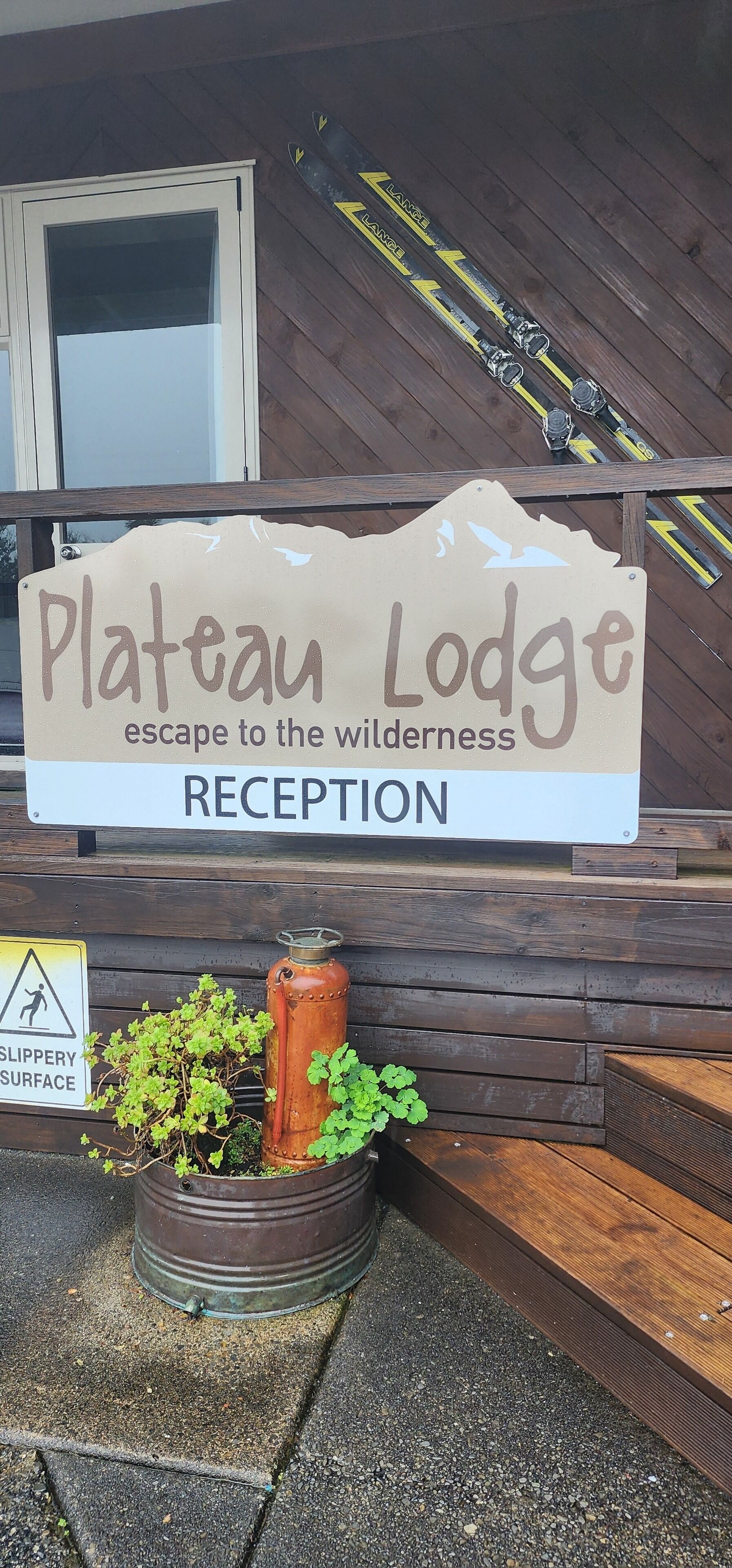 A sign for Plateau Lodge Reception with a wooden backdrop and skis above.