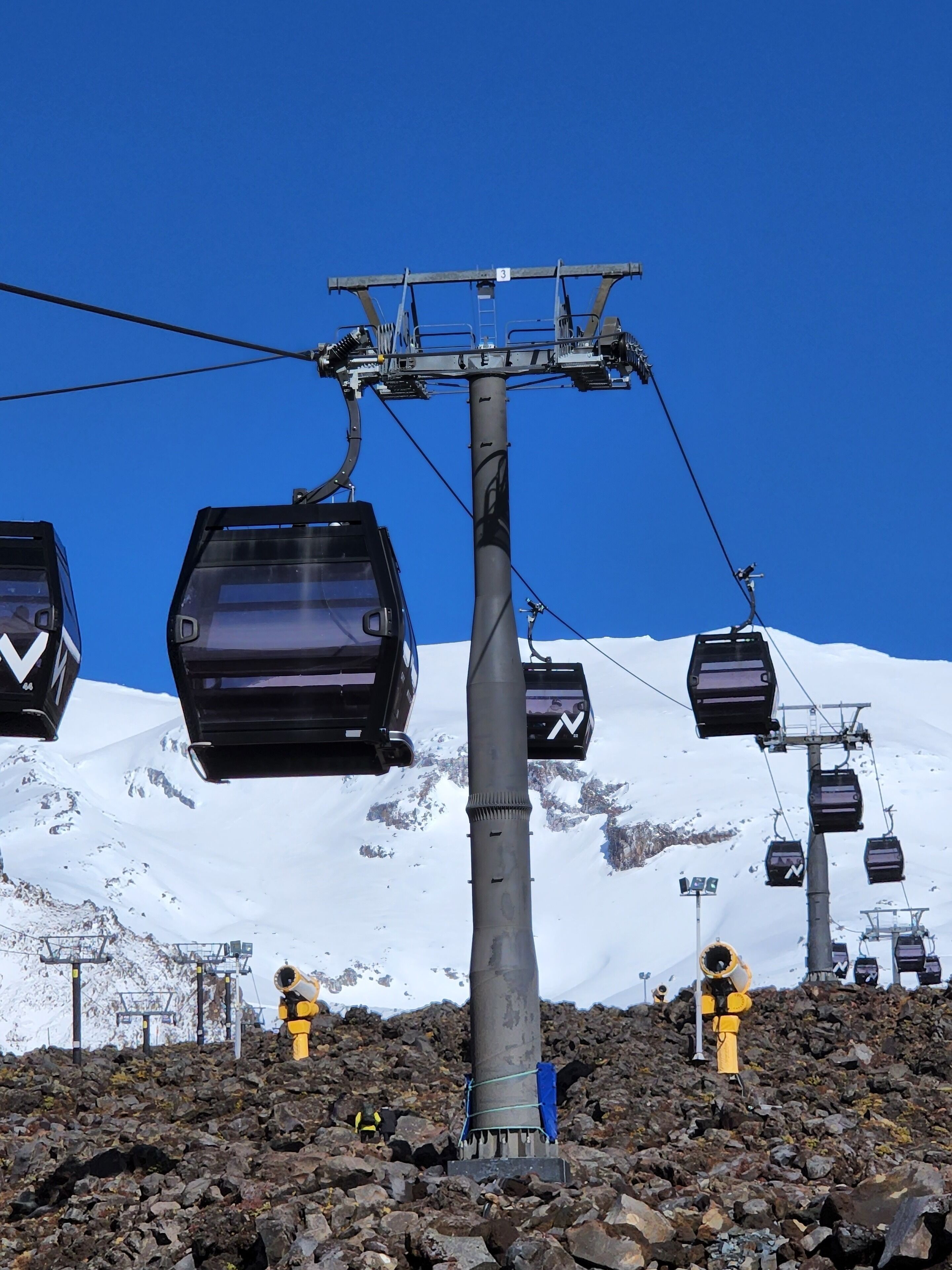 A ski lift with chairs suspended from a central cable, set against a snowy mountain backdrop.