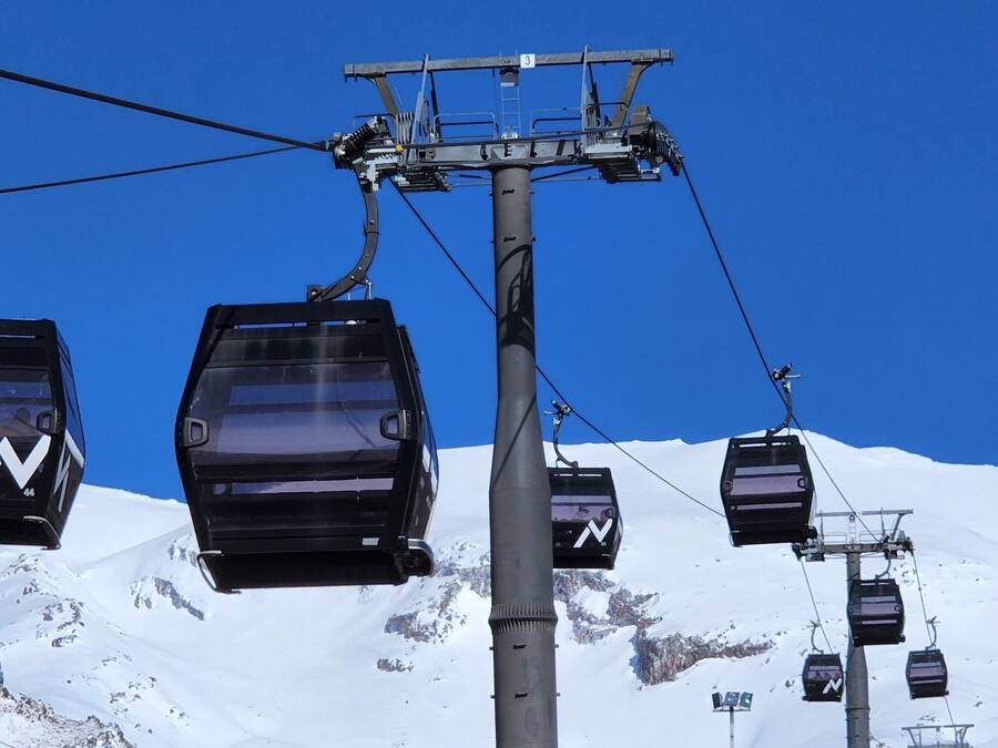 A ski lift with chairs suspended from a central cable, set against a snowy mountain backdrop.