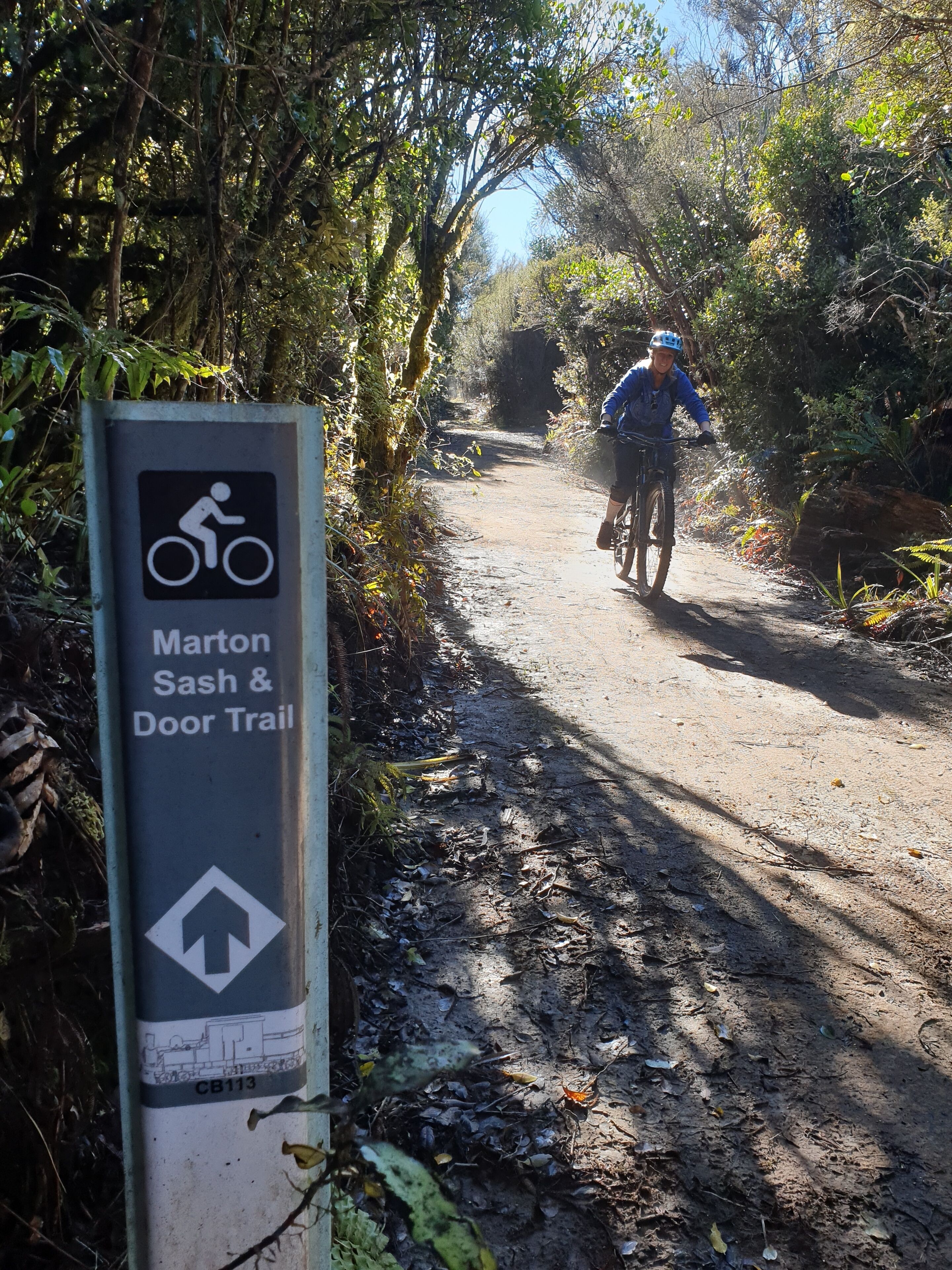 A sign for the Marton Sash & Door Trail with a cyclist in the background.
