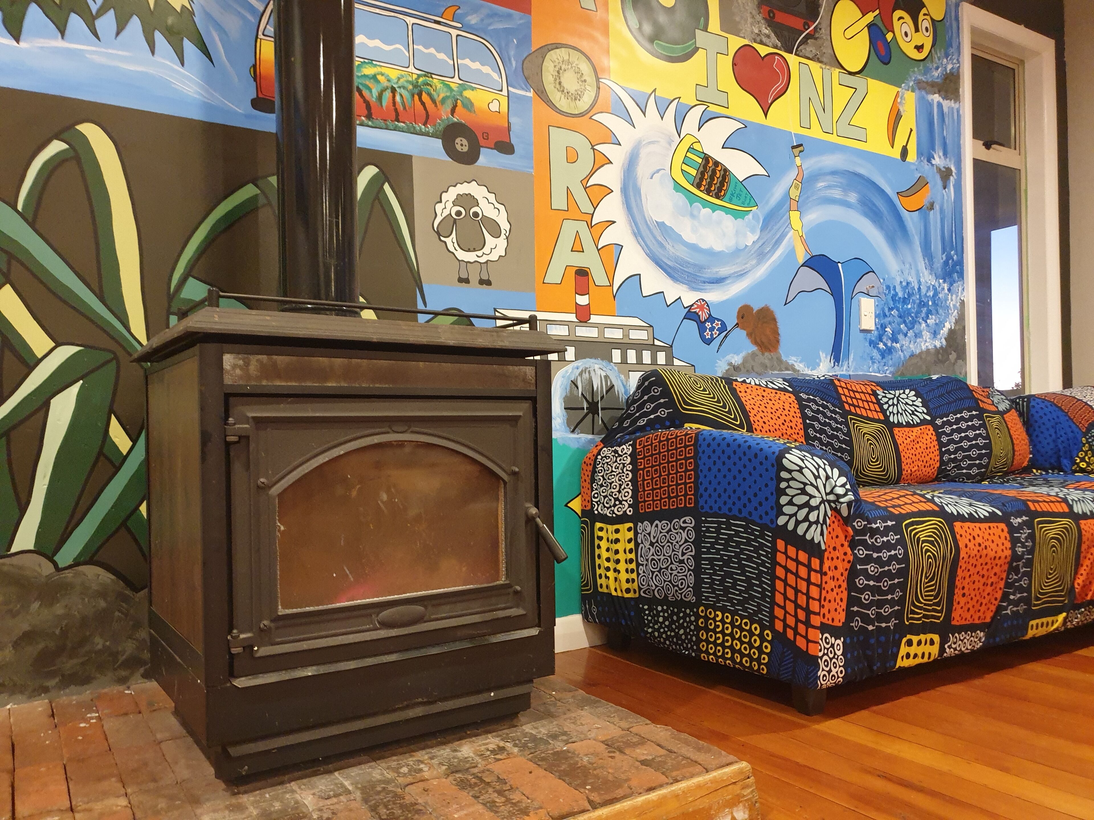A cozy room with a wooden stove, a colorful quilted sofa, and a vibrant mural on the wall.
