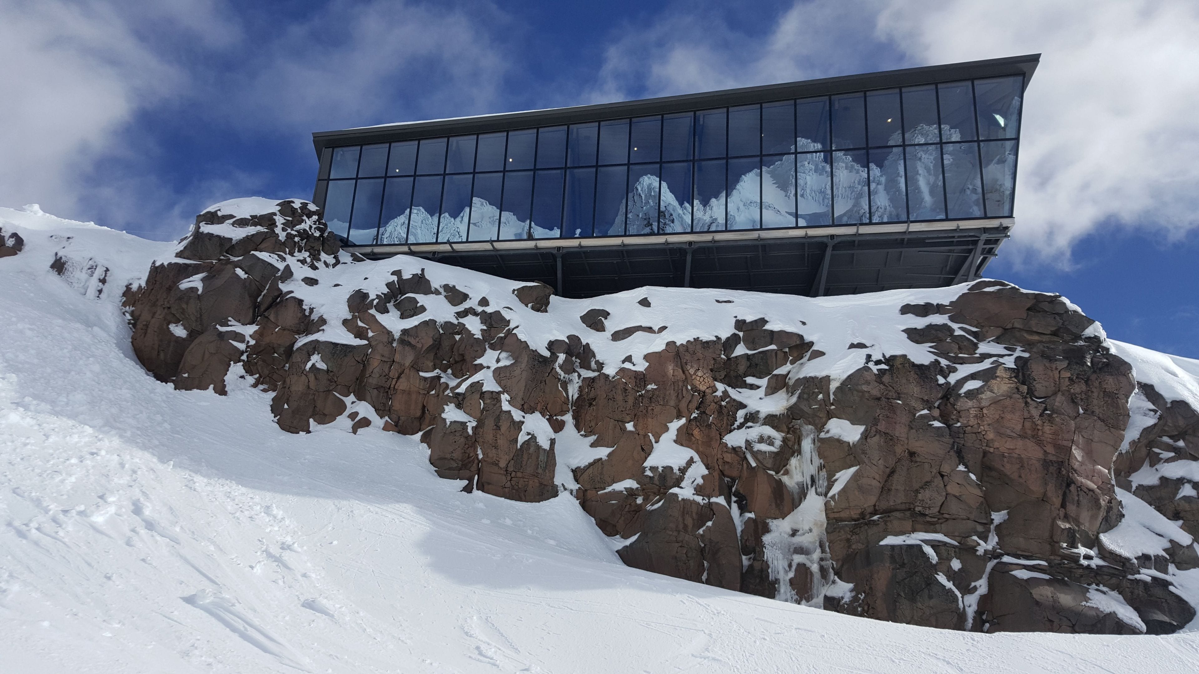 Un edificio moderno con amplios ventanales que reflejan un paisaje montañoso nevado.