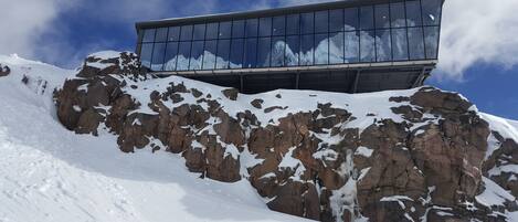 Un edificio moderno con amplios ventanales que reflejan un paisaje montañoso nevado.