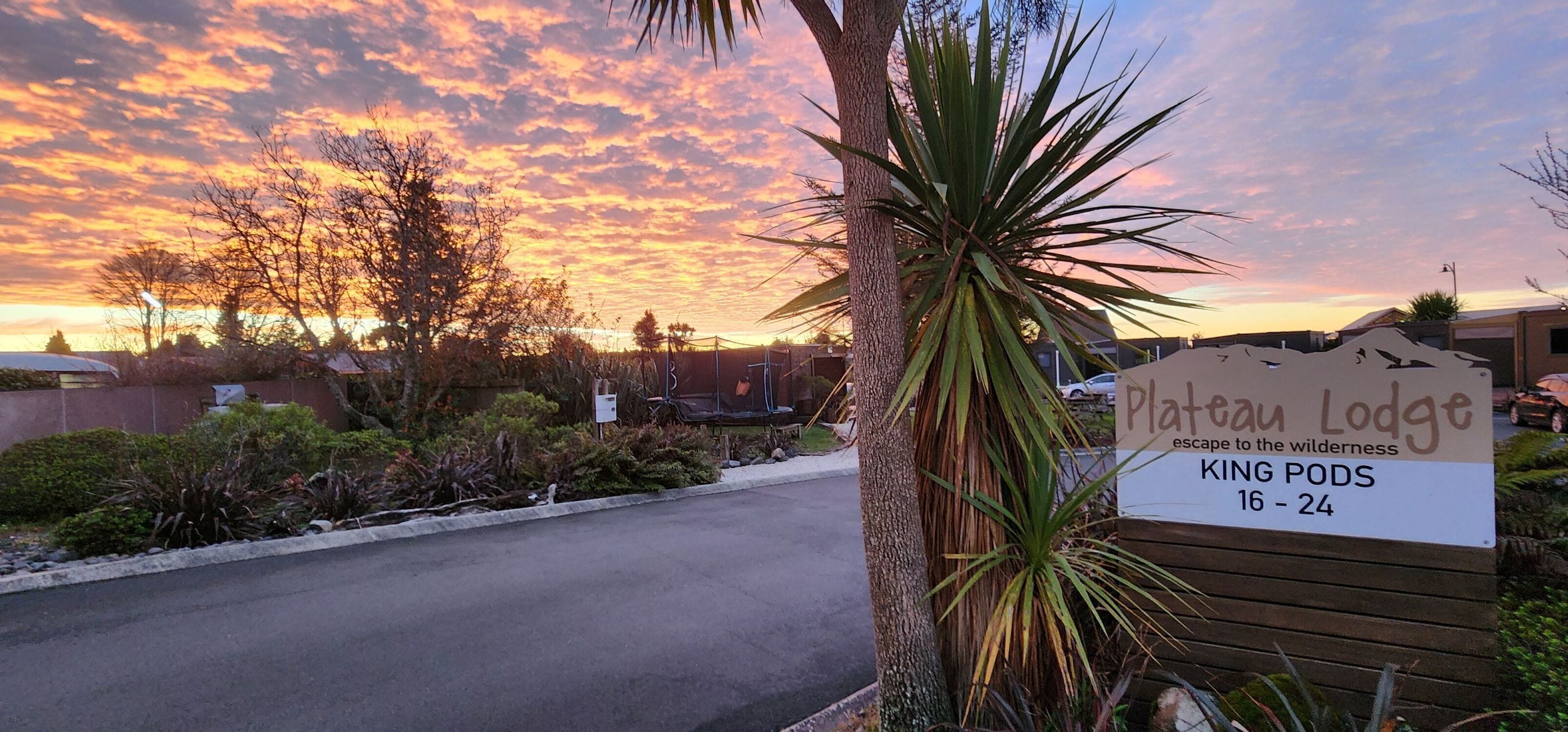 A sign for Plateau Lodge with a view of a sunset and a parking area.
