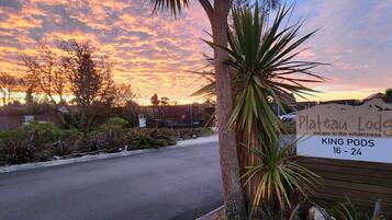 A sign for Plateau Lodge with a view of a sunset and a parking area.