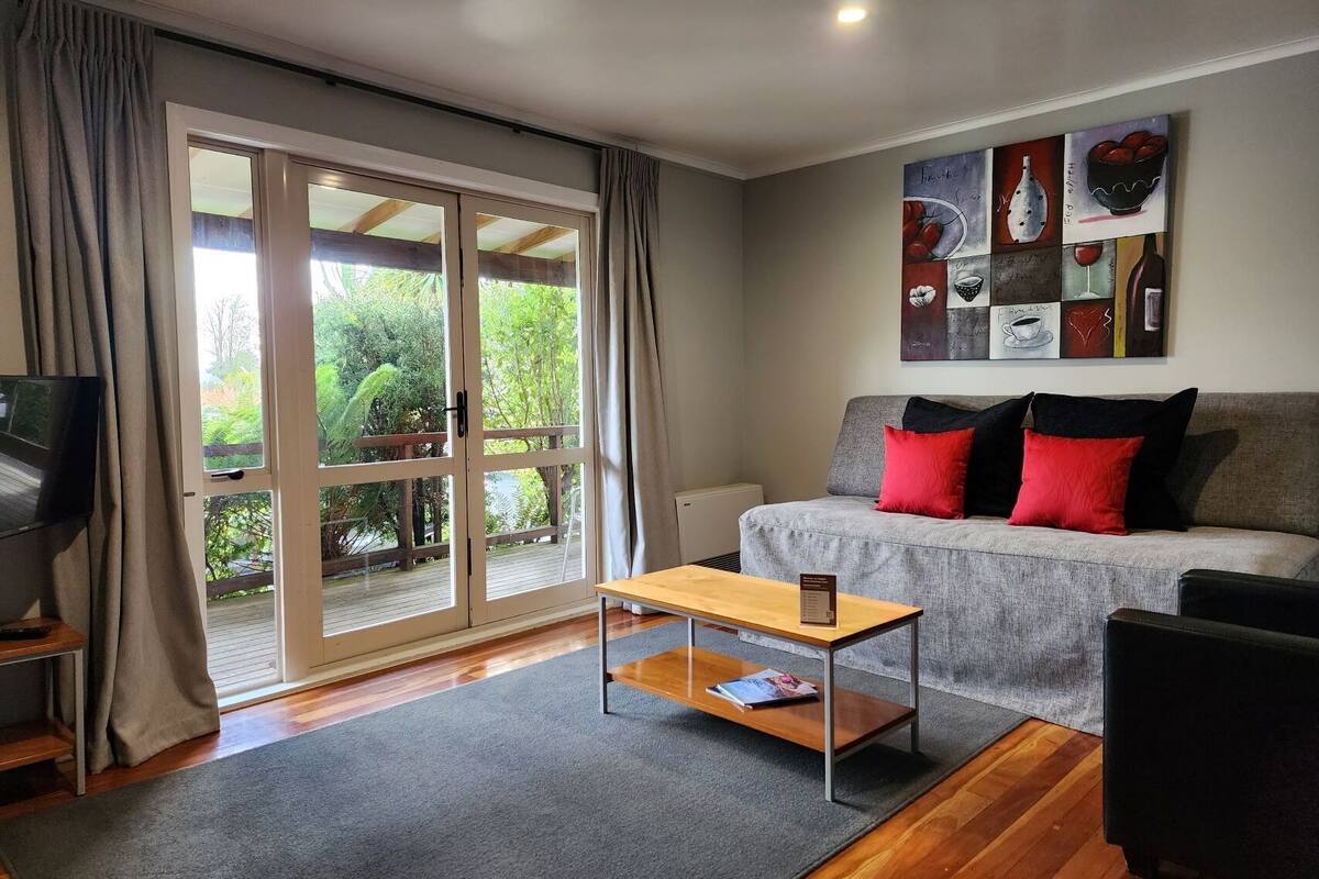 A living room with a grey sofa, red and black cushions, a wooden coffee table, and a TV on a stand.