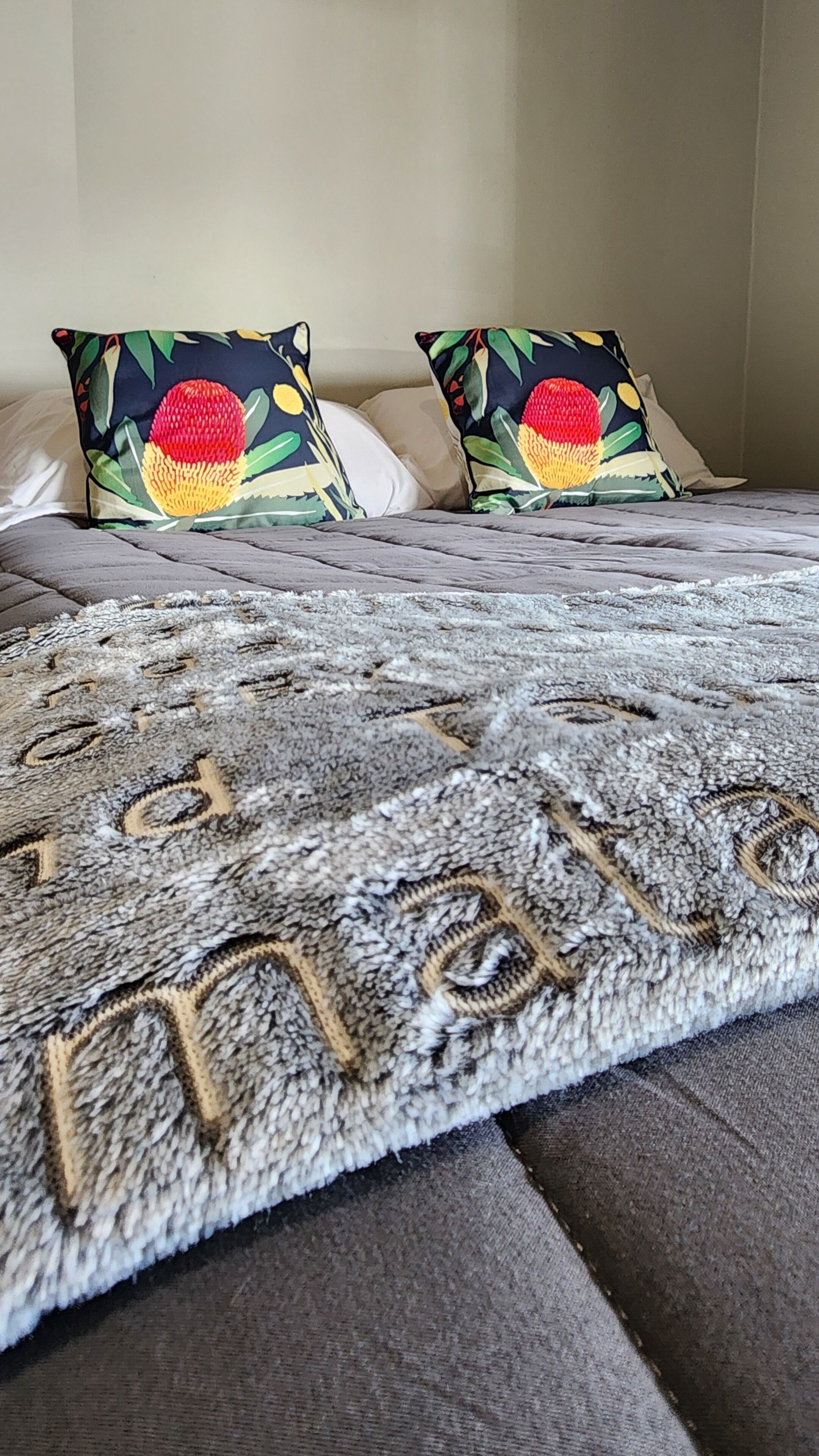 A bed with a grey textured blanket and two pillows with a fruit and leaf pattern.