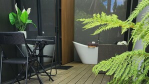 Une terrasse ensoleillée avec un coin salon, une grande fenêtre et des plantes d’intérieur.