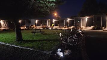 Een nachtzicht van een hotel met meerdere verlichte kamers, een gazon en een bank.