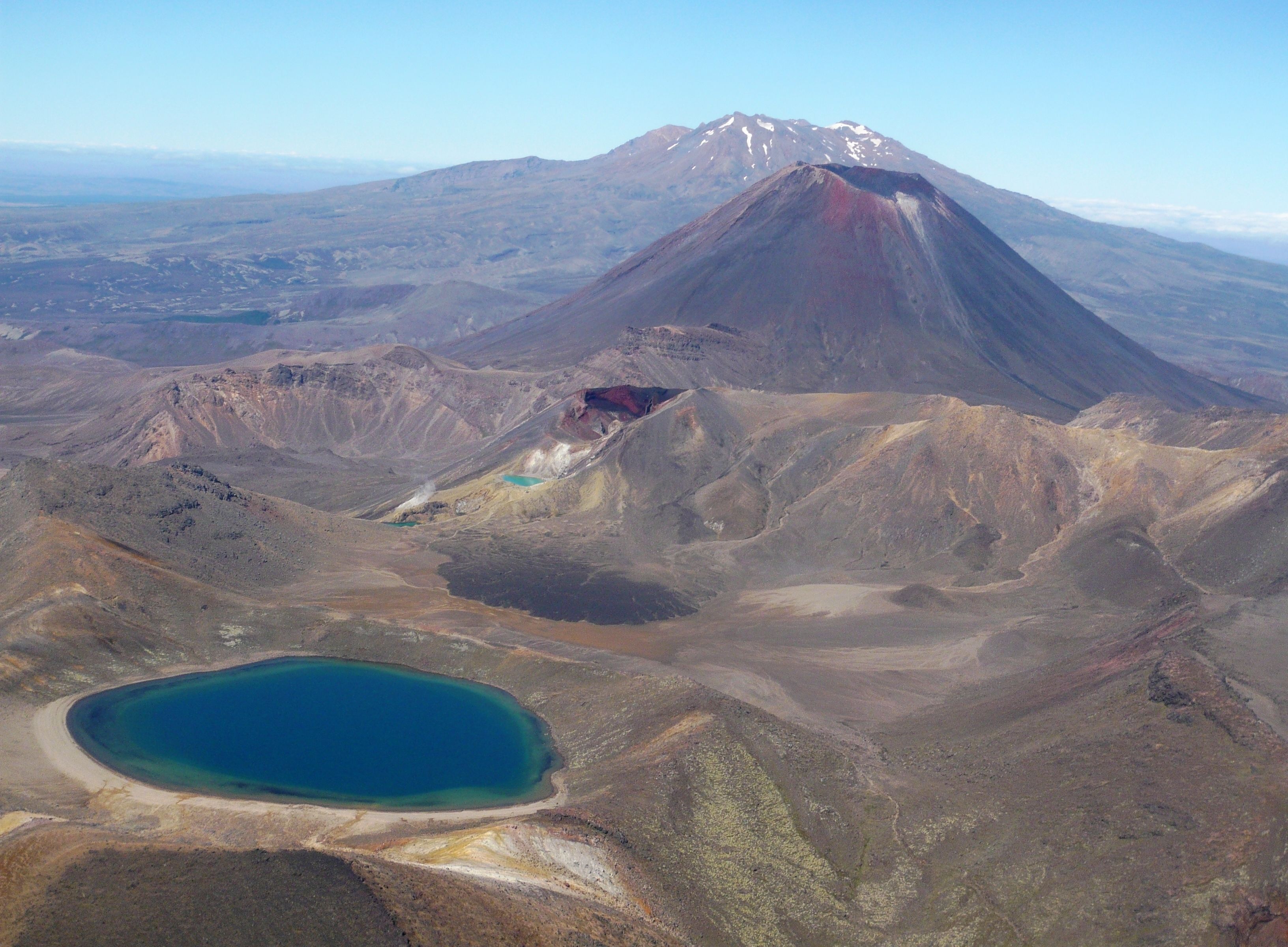 Paisaje volcánico con un lago en un cráter y una montaña al fondo.