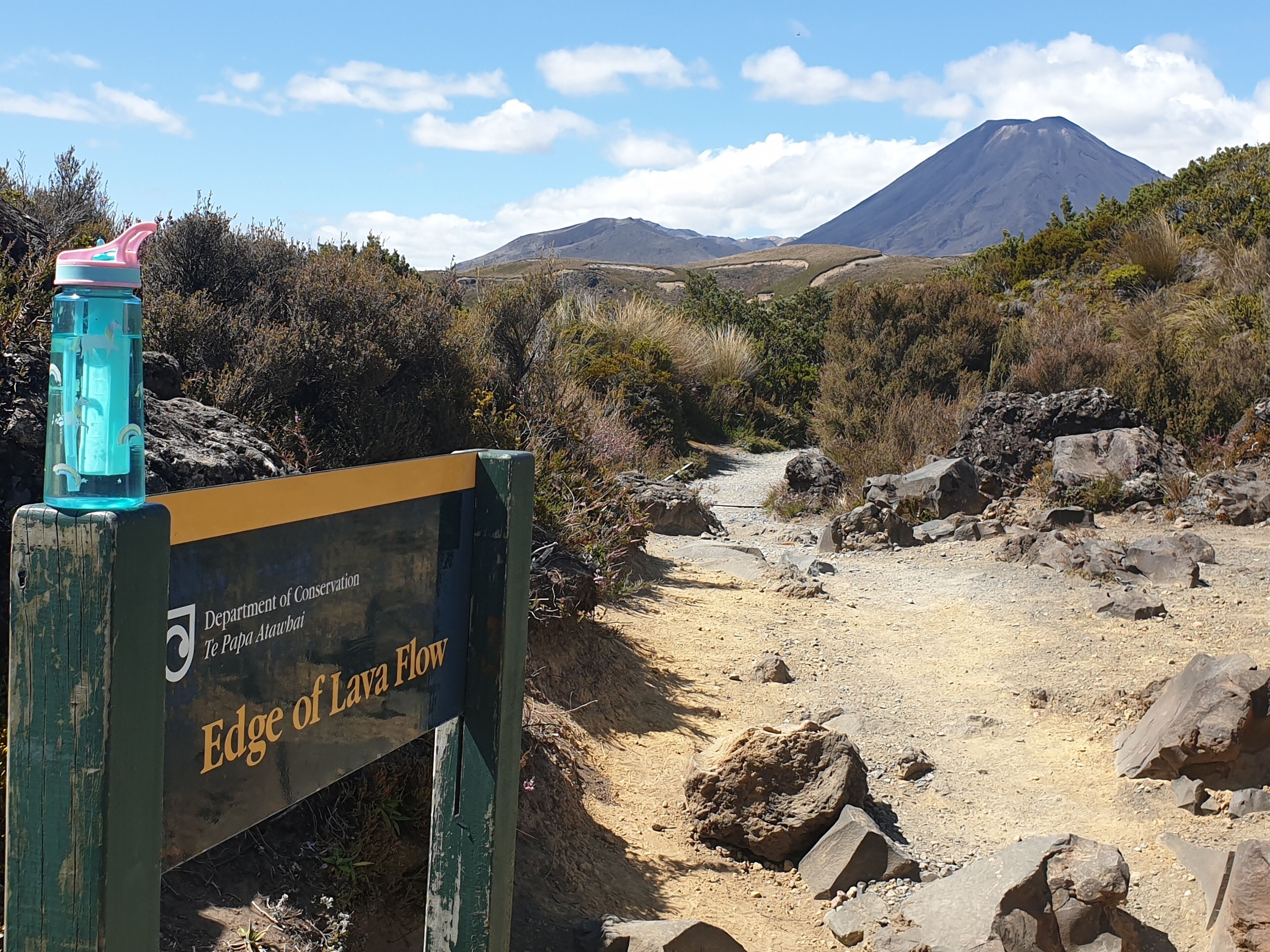 Señal al borde de un flujo de lava con una montaña al fondo.