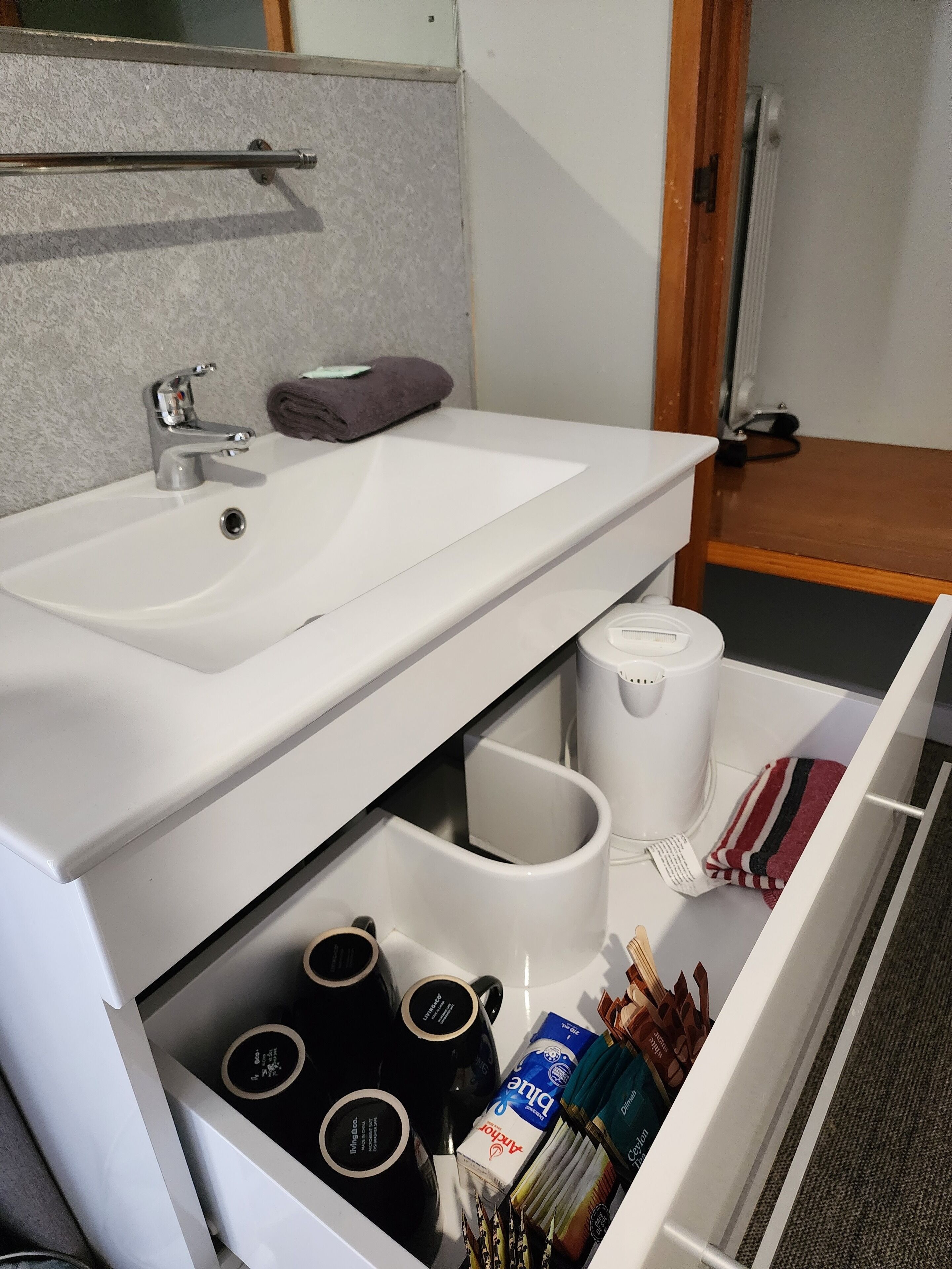 Un baño con lavamanos blanco, toallero y un cajón con artículos de aseo.