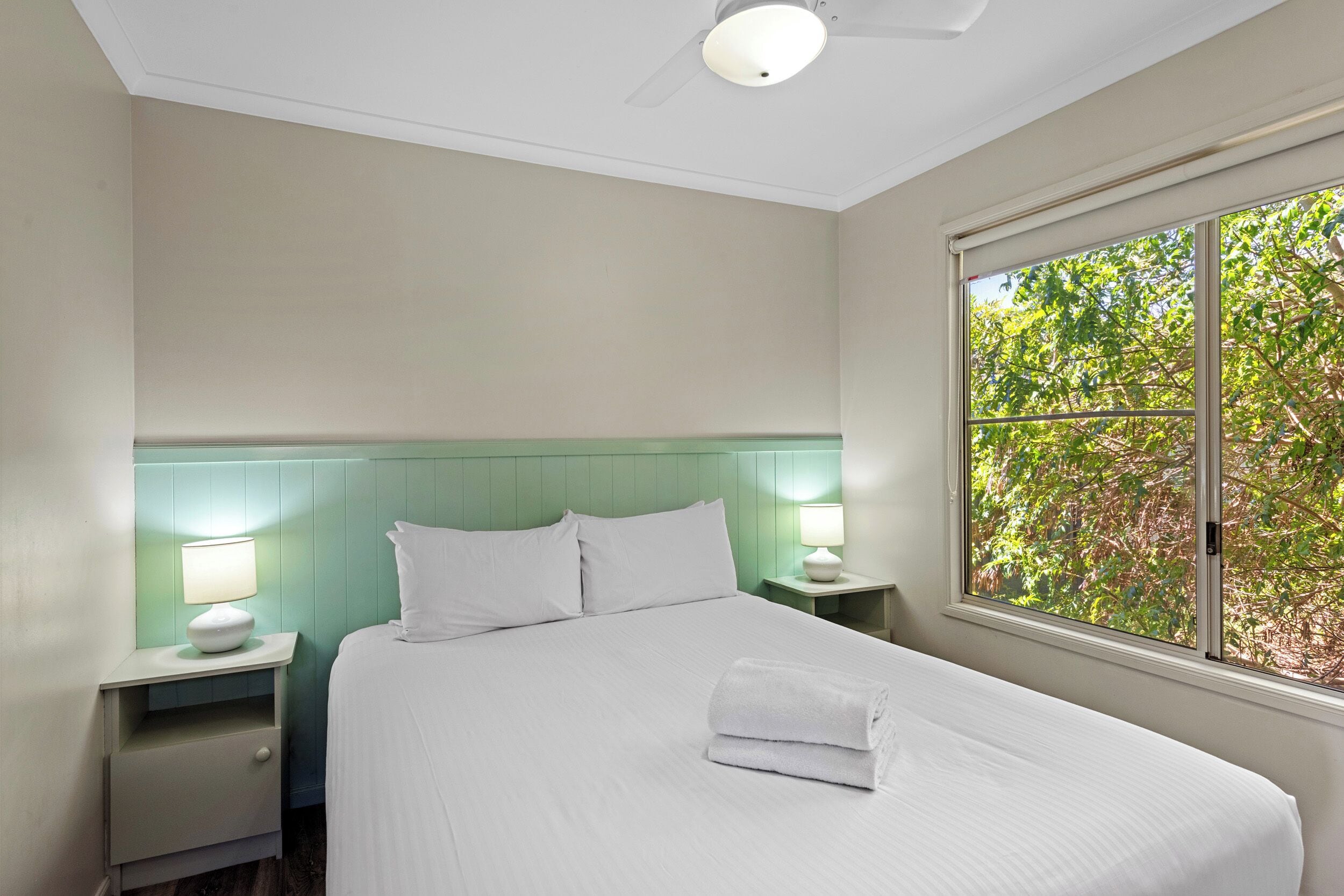 A neatly made bed with white linens, a green headboard, and two bedside lamps.
