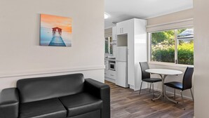 Una cocina moderna con armarios blancos, un comedor con una mesa redonda y dos sillas, y un cuadro de un muelle en la pared.