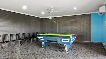 Una sala biliardo con tavolo da biliardo, sedie, una ventola a soffitto e una porta con segnale di uscita.
