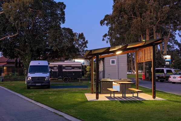 A bus stop with a shelter, benches, and a table. A white van is parked nearby. - Discovery Parks - Perth Airport (Forrestfield)
