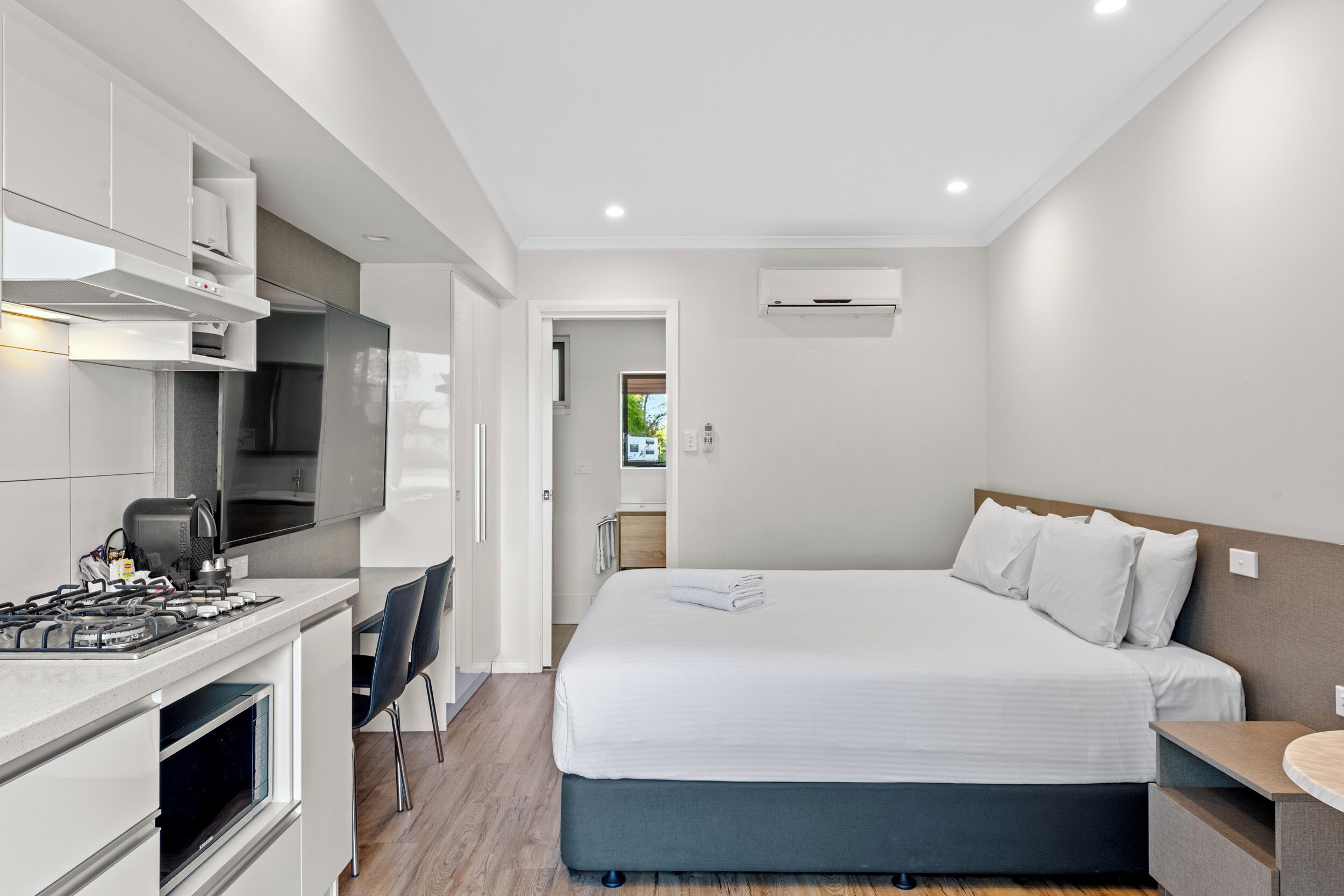 Habitación de hotel moderna con kitchenette, una cama y un baño visible a través de una puerta abierta.