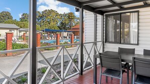 Un espacio al aire libre cubierto con piscina, una mesa y sillas, y vistas a un parque infantil y árboles.