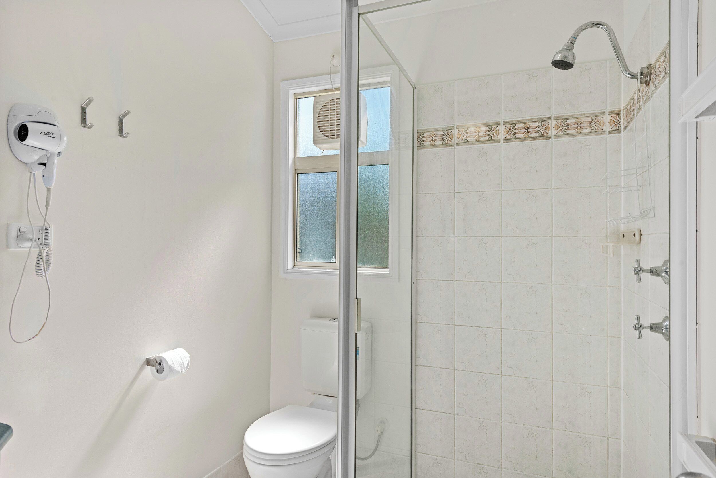 A bathroom with a toilet, a shower, and a hairdryer mounted on the wall.