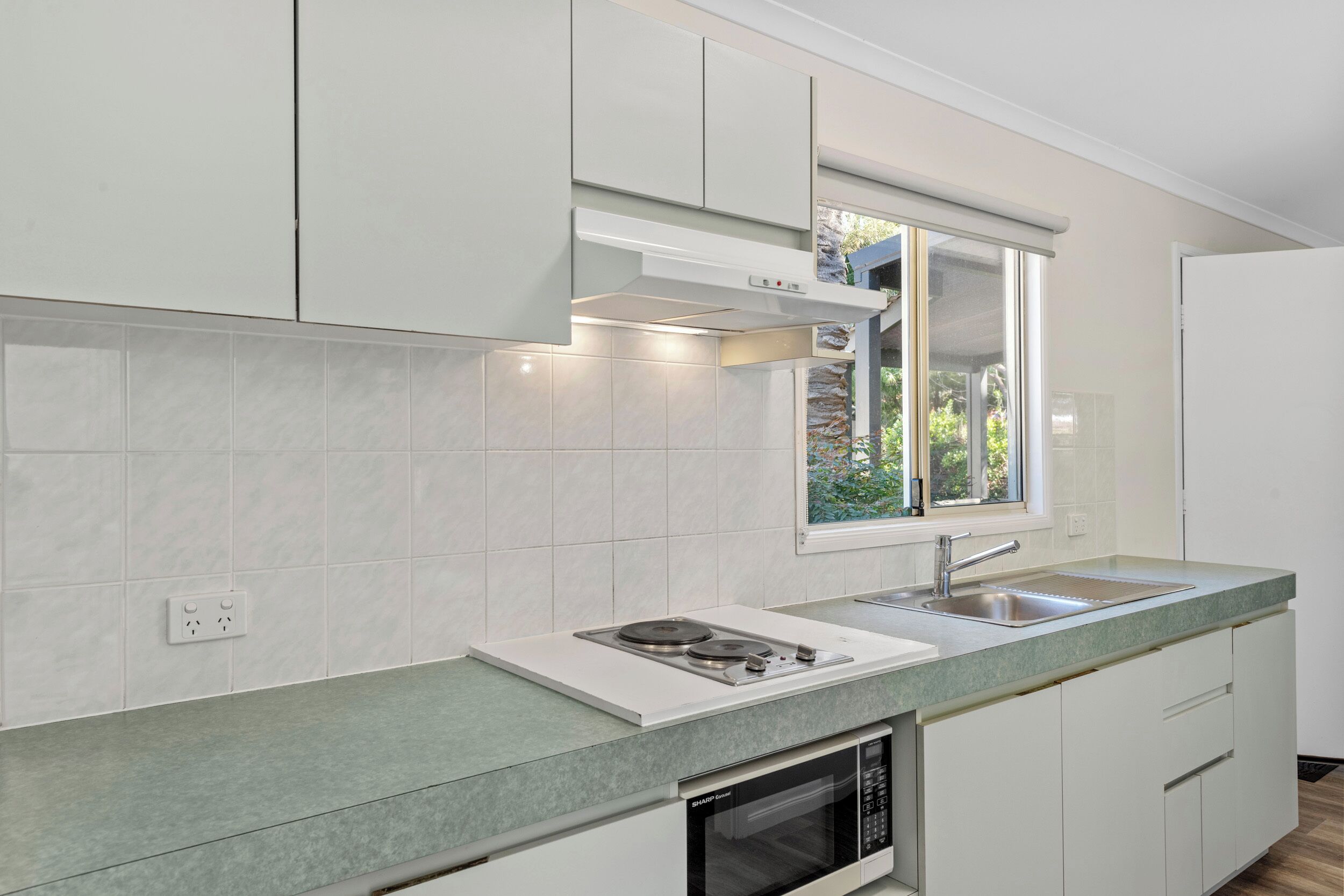 Una cocina moderna con armarios blancos, microondas integrado y ventana sobre el fregadero.