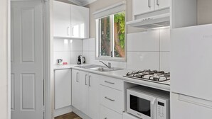 Una cocina moderna con armarios blancos, un lavamanos de acero inoxidable, una estufa a gas y un microondas.