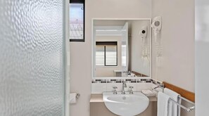 A bathroom with a white sink, two faucets, a mirror, and two hair dryers mounted on the wall.