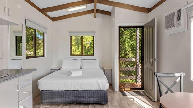 Un dormitorio con una cama, una mesita de noche, un aparador, un ventanal y una puerta que da a un balcón.