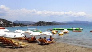 A beach with sun loungers and umbrellas, a rocky shoreline, and a distant iceberg. - Paradise Lost Hotel-Apartments (Nafplio)