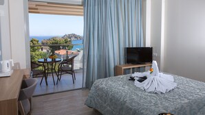 A hotel room with a balcony, a bed, a desk, a chair, a TV, and a table with a view of the sea and hills. - Paradise Lost Hotel-Apartments (Nafplio)