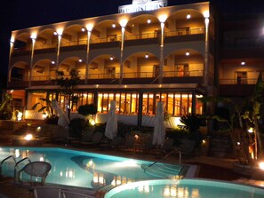 A hotel with a pool area, outdoor seating, and a well-lit facade.
