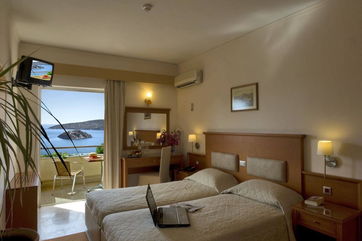 Een hotelkamer met twee bedden, een bureau, een stoel, een laptop en een televisie.